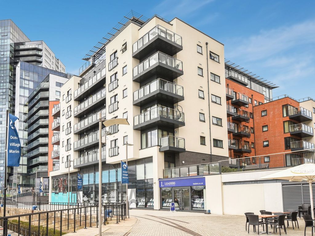 Modern apartment building with balconies and ground floor shops beside a waterside walkway